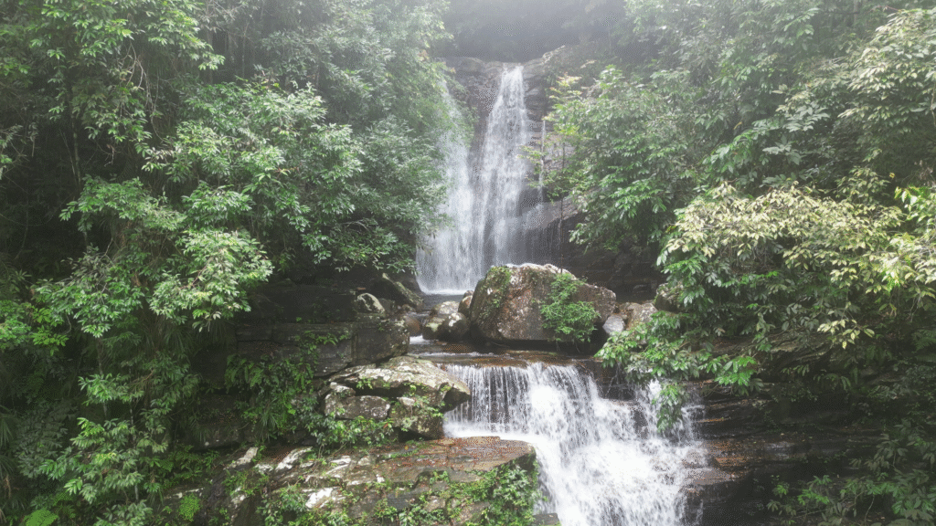 Close-up of the upper tier of a cascading waterfall, showing the forceful white water rushing over ancient dark rock formations