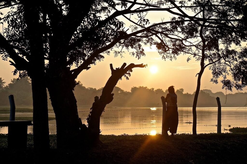 A breathtaking sunset over Ridiyagama Lake, with the sky painted in hues of deep orange and gold reflecting off the calm water surface